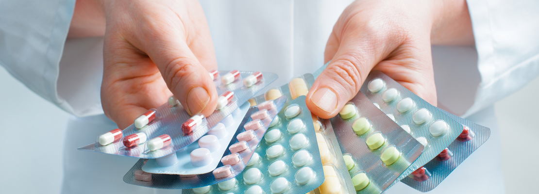 Person in weißem Kittel hält mehrere Blister mit Pillen und Tabletten in den Händen.